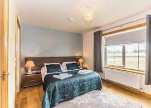 Ein Schlafzimmer mit Bett, Nachttischlampen, einem Fenster mit Vorhängen, einer Heizung und einem Holzboden.