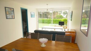 Un coin repas avec une table en bois, des chaises, un banc et un téléviseur en arrière-plan.