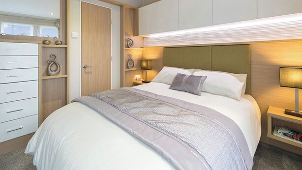 Une chambre d’hôtel comprenant un lit, des tables de chevet, une armoire et une tête de lit dotée d’un éclairage intégré.