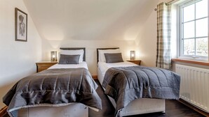 A bedroom with two beds, a window with curtains, a radiator, and a framed picture on the wall. - 4 bedroom accommodation in Hornsea (Hornsea)