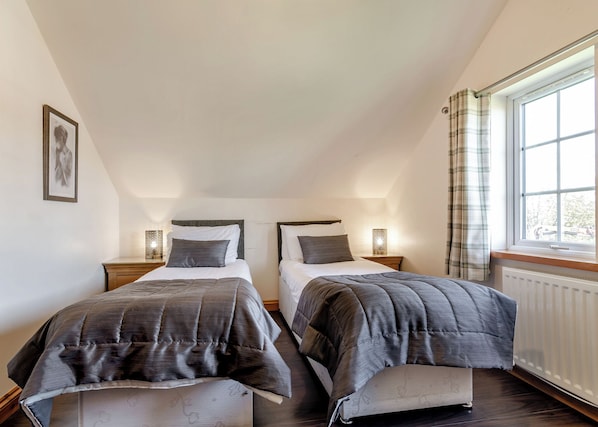 A bedroom with two beds, a window with curtains, a radiator, and a framed picture on the wall.