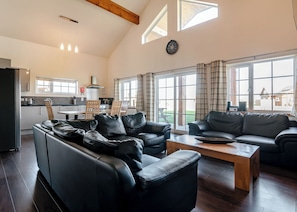 A spacious living room with a black leather sofa, a wooden coffee table, and a kitchen in the background.