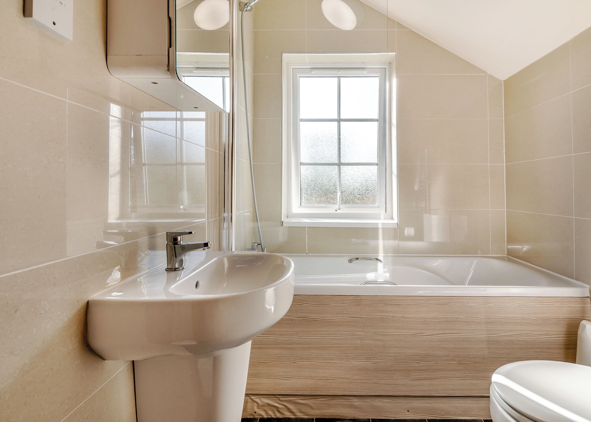 A bathroom with a sink, mirror, window, and bathtub.