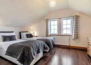 Quarto com duas camas, um radiador, uma janela com cortinas e piso de madeira.