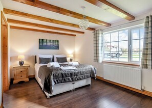 Quarto com cama, luminárias de cabeceira, janela com cortinas, radiador e um quadro na parede.
