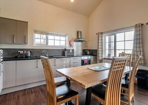 A modern kitchen with a wooden dining table and chairs, a built-in oven, and a window with curtains.