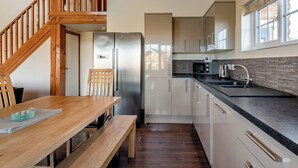 A modern kitchen with wooden staircase, stainless steel appliances, and a dining area with a wooden table and bench. - 4 bedroom accommodation in Hornsea (Hornsea)