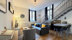 Un espacio de estar moderno con sofá, mesa de centro, comedor con sillas, una escalera y vistas al exterior.
