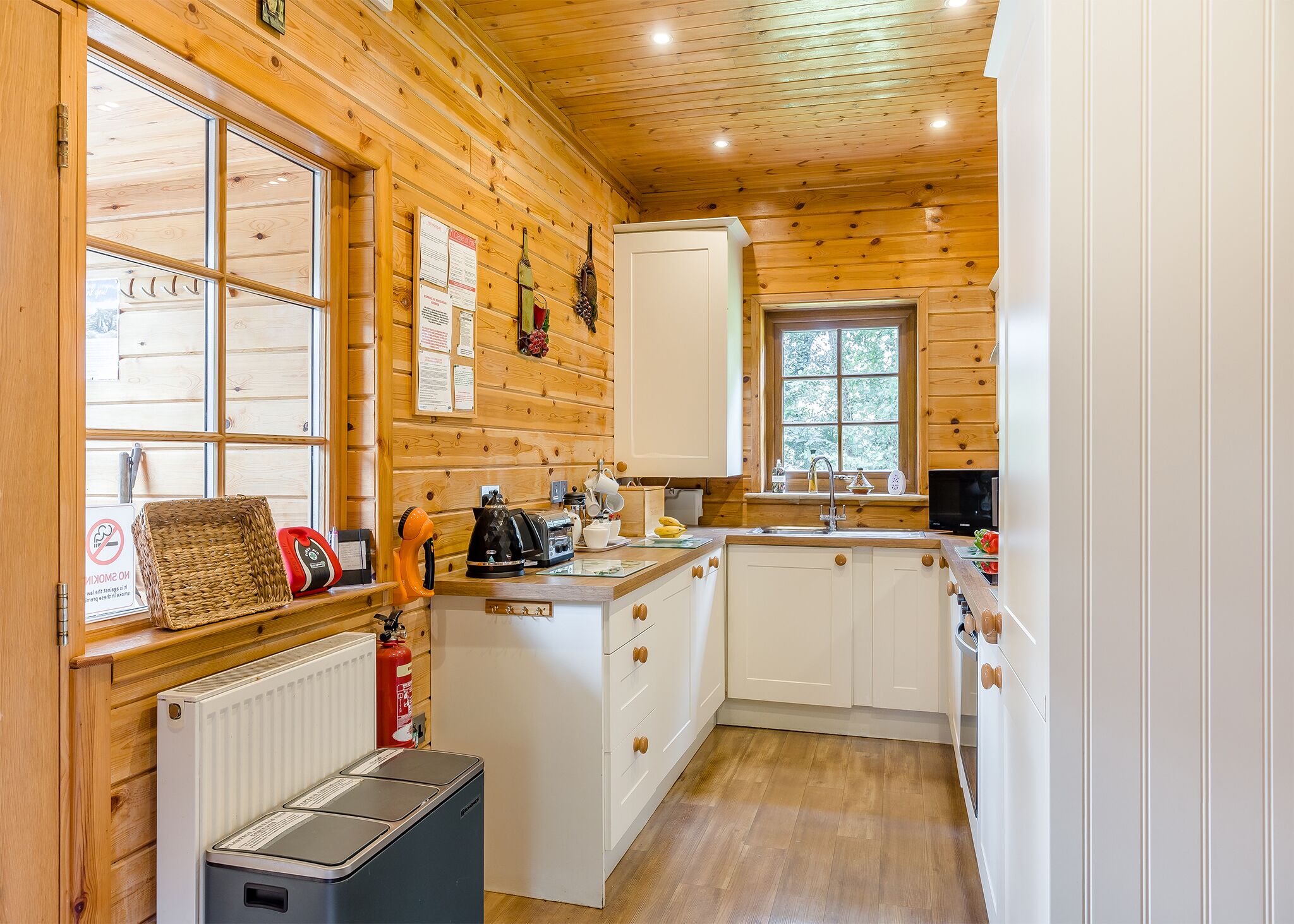 Una cocina pequeña con paredes de madera, armarios blancos, una ventana y un radiador.