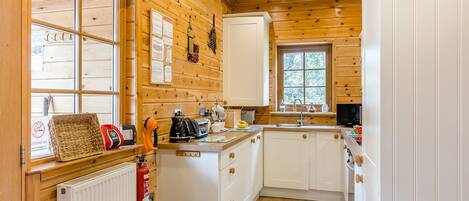 Una cocina pequeña con paredes de madera, armarios blancos, una ventana y un radiador.