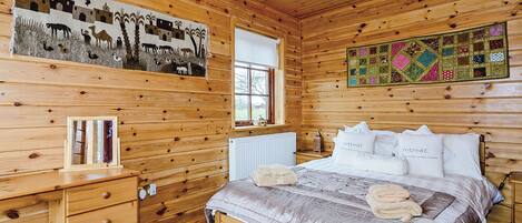 A wooden cabin bedroom with a bed, a dresser, a window, and a wall mural.