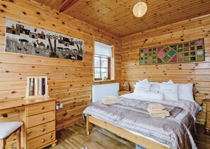 Dormitorio de una cabaña de madera con cama, cómoda, ventana y un mural en la pared.