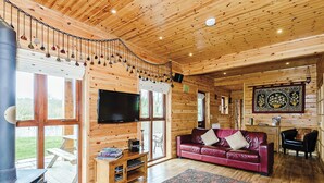 Een interieur van een chalet met houten plafond, een televisie, een rode leren bank, een open haard en een eethoek.