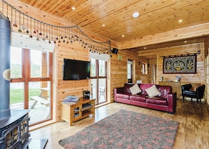 A cabin interior with a wooden ceiling, a television, a red leather sofa, a fireplace, and a dining area.