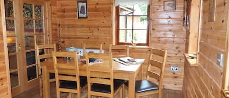 A wooden cabin interior with a dining table, chairs, a window, and a door with glass panels.