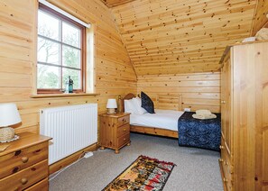 A wooden cabin room with a bed, dresser, and window.