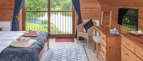 Quarto de cabana de madeira com uma cama, uma escrivaninha, uma cadeira, um armário e uma televisão.