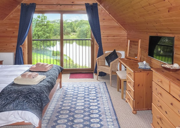 A wooden cabin room with a bed, a desk, a chair, a dresser, and a TV.