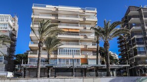 Un hôtel à plusieurs étages doté de balcons, de palmiers et d’un restaurant situé au rez-de-chaussée.
