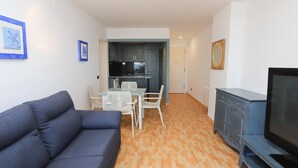 Un salon comprenant un canapé, un téléviseur et un coin repas avec des chaises et une table.