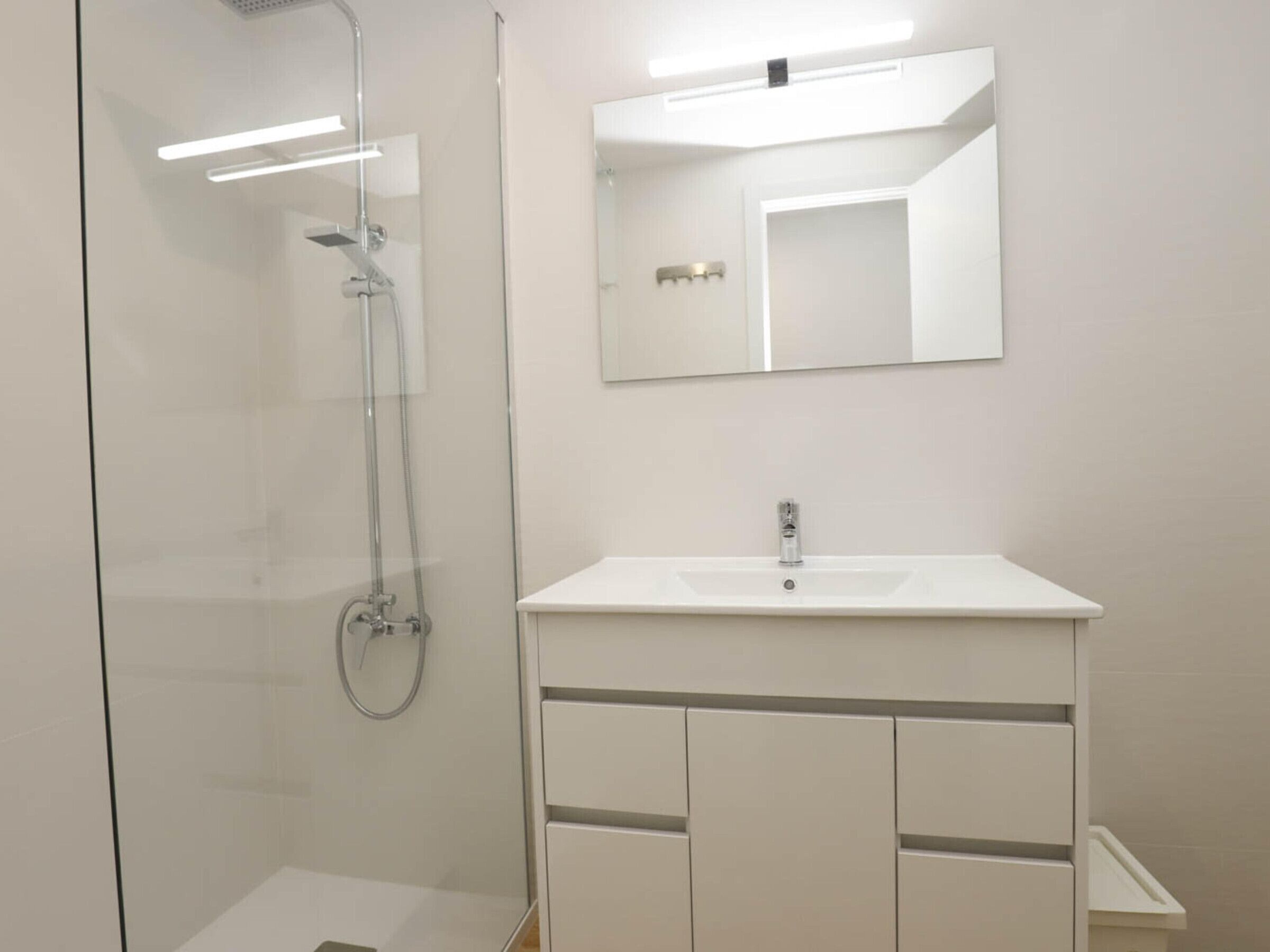 A modern bathroom with a glass-enclosed shower, a white sink with a mirror above it, and a cabinet below.