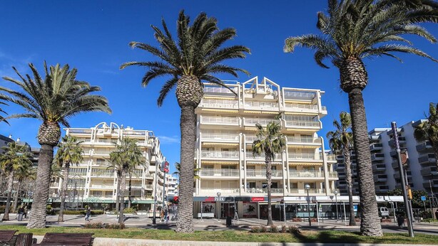 A multi-story hotel with balconies, palm trees, and a paved walkway.