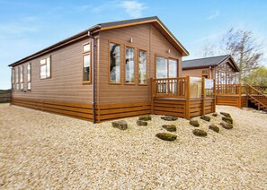 Eine Holzhütte mit Veranda, einer kleinen Terrasse und einem Schotterweg.