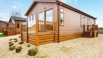 A wooden cabin with a porch, large windows, and a gravel driveway.
