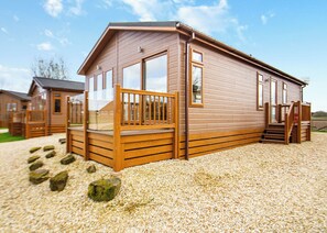 A wooden cabin with a porch, large windows, and a gravel driveway.
