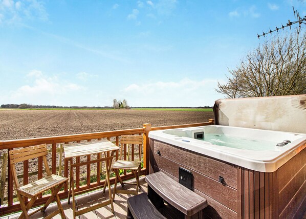 A hot tub on a deck with wooden chairs and a view of a plowed field.
