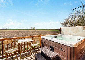 A hot tub on a deck with wooden chairs and a view of a plowed field.