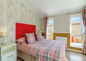 A bedroom with a red headboard, a bed with plaid bedding, a bedside table with a lamp, and a window with curtains.