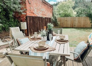 An outdoor patio with a wooden table set for four, surrounded by wicker chairs with patterned cushions.