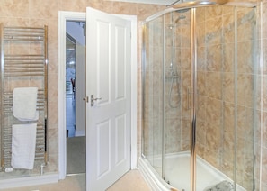 Un baño con ducha de vidrio, una puerta blanca y un perchero con toallas blancas.