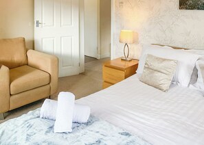 Una habitación de hotel con cama, una silla, una mesita de noche con lámpara y una puerta.