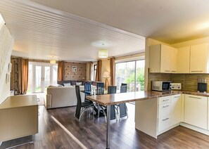 A modern kitchen with a dining area, wooden flooring, and large windows.