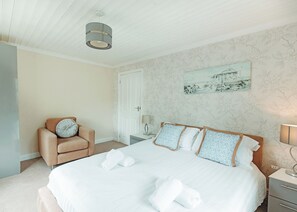 A bedroom with a bed, a chair, a nightstand, a lamp, and a painting on the wall.