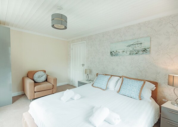 A bedroom with a bed, a chair, a nightstand, a lamp, and a painting on the wall.