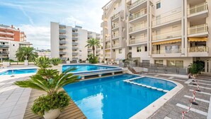 Un hotel moderno con una piscina central, varios balcones y un área exterior bien cuidada con palmeras.
