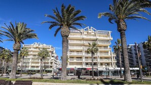 Un hotel de varios pisos con balcones, palmeras y un camino pavimentado.