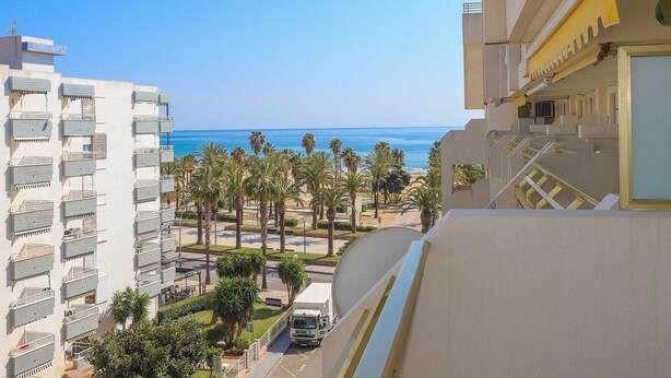 Un edificio de gran altura con balcones que dan a una playa y palmeras.