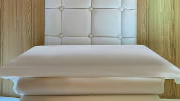 Una cama con cabecera acolchada y cubrecama blanco impecable.