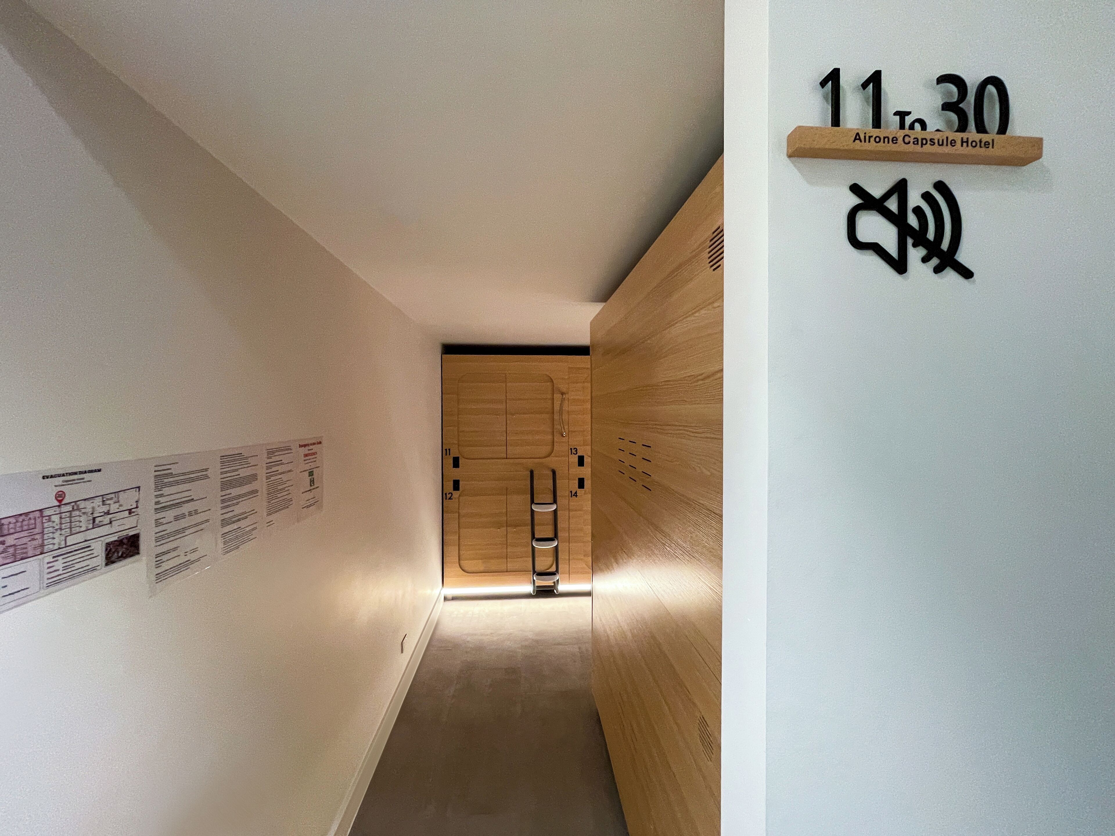 A hallway with a wooden door, numbered 11 to 30, and a sign indicating the Airone Capsule Hotel.