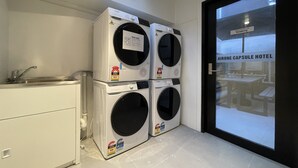 A laundry area with stacked washing machines and a sink. - Airone Capsule Hotel (Hobart)