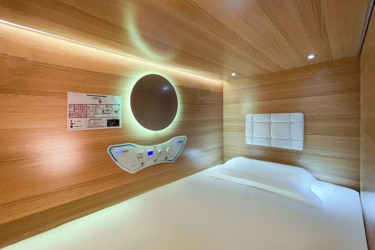 A modern hotel room with a wooden ceiling, a control panel, a circular mirror, and a bed.