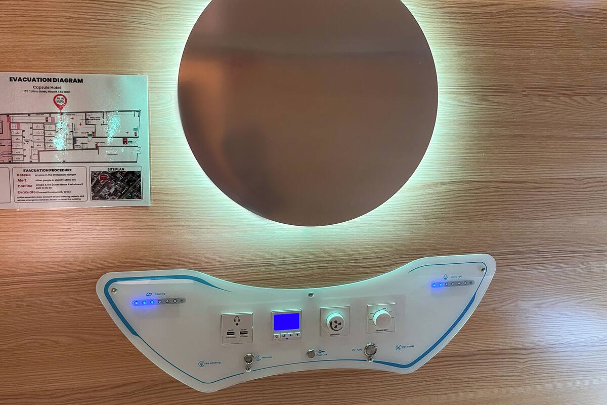 A hotel room with a large mirror, a control panel with various settings, and an evacuation diagram on the wall.