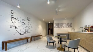 A modern kitchen with marble flooring, wooden benches, and a round table with chairs. A large wall map is visible, and the word "AIRONE" is displayed prominently. - Airone Capsule Hotel (Hobart)