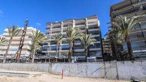 Un edificio de varios pisos con balcones, palmeras y un primer plano de arena.