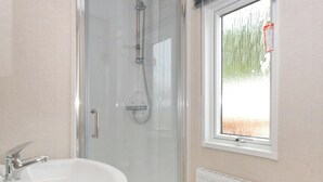 A bathroom with a glass-enclosed shower, a white sink, and a window with a view of trees.