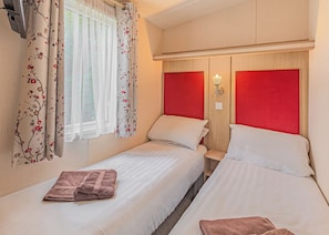 A double room with two beds, a window with sheer curtains, a wall-mounted light, and a wooden headboard.